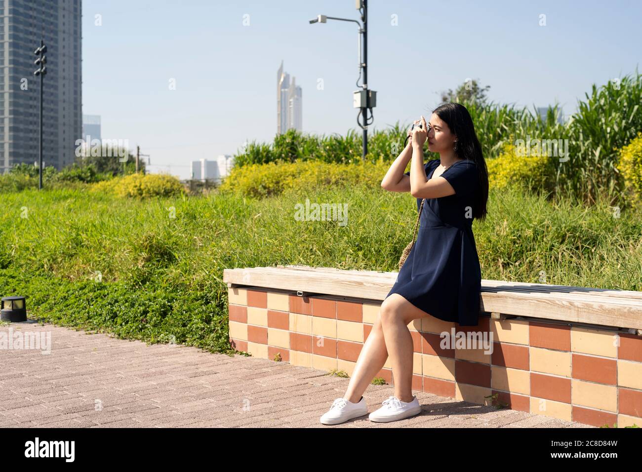 Long hair woman in dark blue dress sitting on the bench in the park and ...