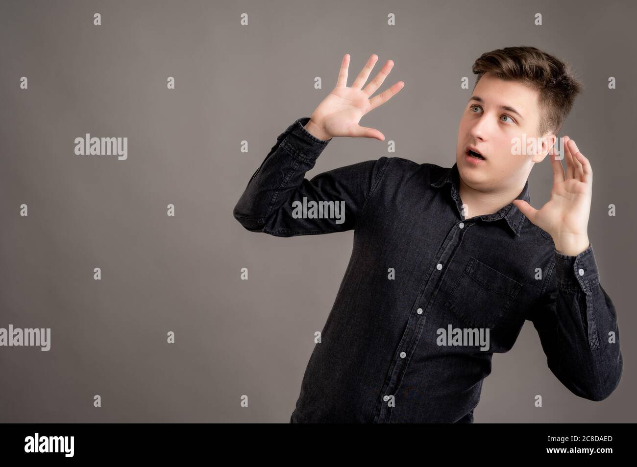 Portrait of serious stylish attractive man dressed with a casual black shirt making scary gesture isolated on grey background with copy space advertis Stock Photo