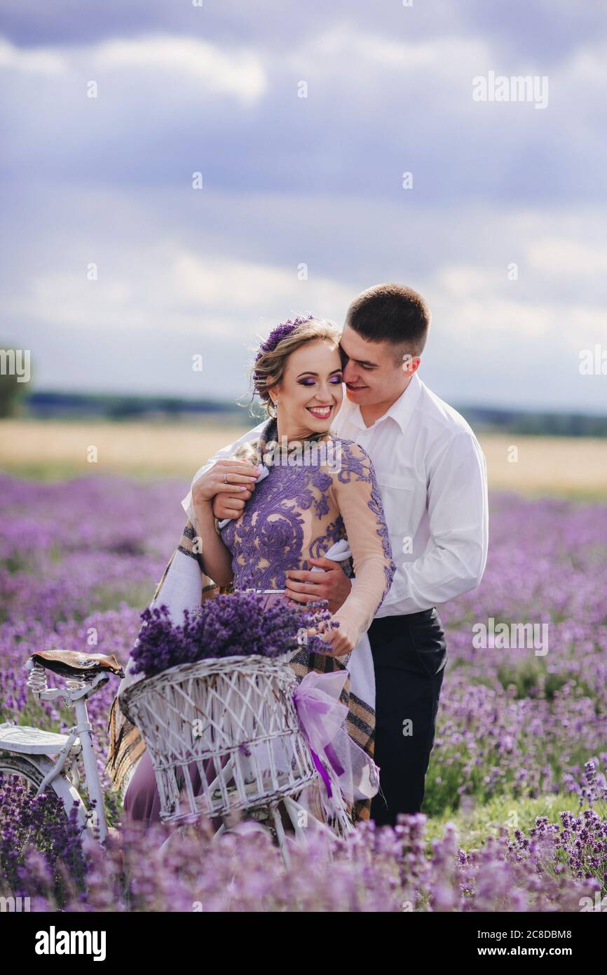 Happy young couple are walking with retro bicycle in lavender field. man is  hugging her woman in purple dress and with hairstyle outdoors Stock Photo -  Alamy