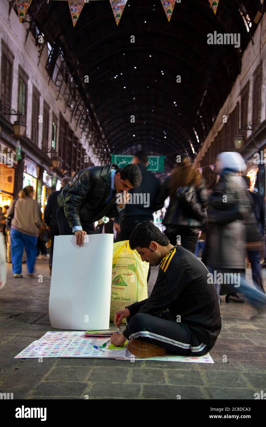 Damascus, Syria 03/28/2010: A young Syrian man is sitting cross legged on the floor of the crowded Al-Hamidiyah Souq, trying to sell cheap plastic dra Stock Photo