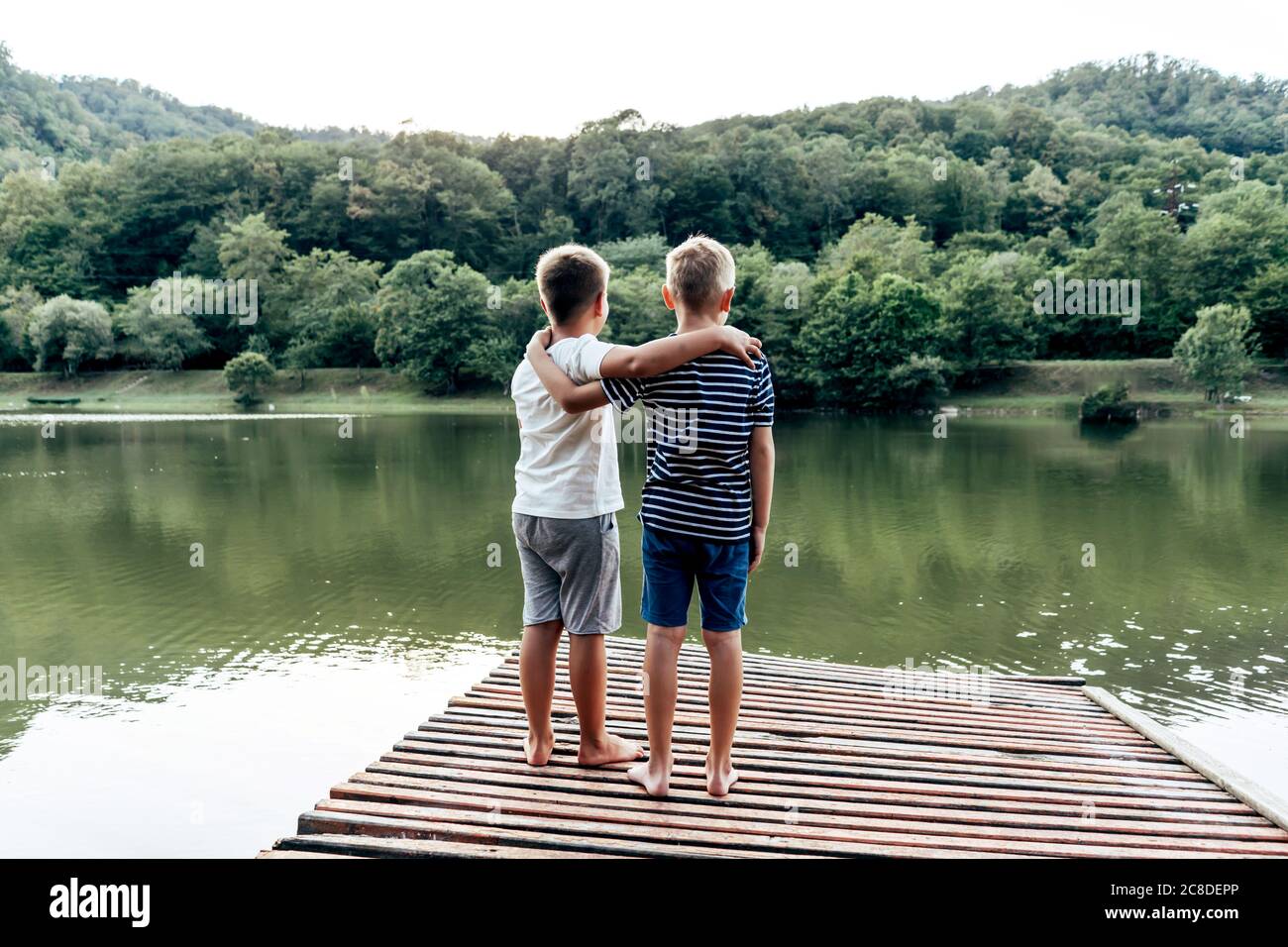 Two boys stand on the pier by the lake. Stock Photo