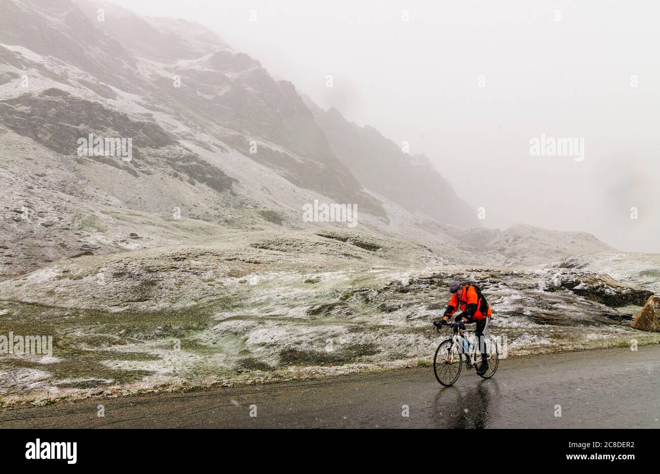 Cyclist in snowfall during summer on a mountain road climbing the famous Col de l'Iseran in the French Alps Stock Photo