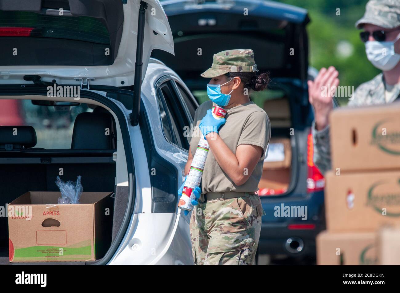 U.S. Army Pfc. Stephanie Huertas, a motor transport operator with the Delaware Army National Guard's 1049th Transportation Company, carries a stack of cans at a drive-thru food pantry on the grounds of Dover International Speedway in Dover, Delaware, June 24, 2020. About 25 soldiers and airmen of the National Guard joined volunteers with the Food Bank of Delaware there, distributing much-needed pantry items to address the increased demand for food assistance amid COVID-19. (U.S. Army National Guard photo by Capt. Brendan Mackie) Stock Photo