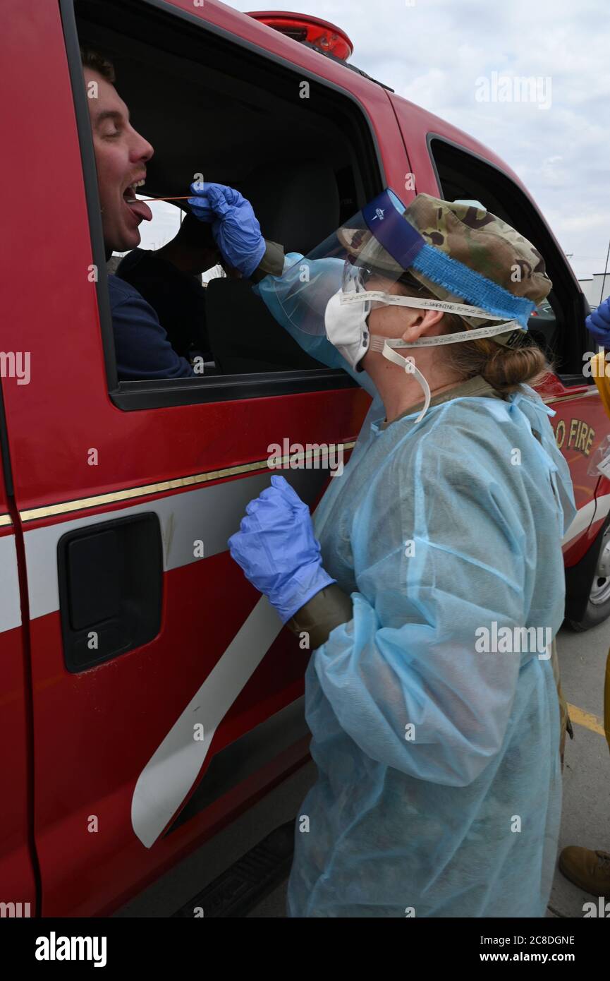 Maj. Shelley Bartow, of the North Dakota National Guard state medical detachment, takes a swab sample from an asymptomatic Fargo Fire Department fire fighter who is volunteering to take a COVID-19 test in the parking lot of the FaroDome, N.D., April 25, 2020. She is wearing personal protective equipment (PPE) to stay safe while she works and help prevent the spread of the Coronavirus while testing people as they drive through the mass testing process in their vehicles. She is just one of the N.D. National Guard members partnering with the N.D. Department of Health and other civilian agencies i Stock Photo