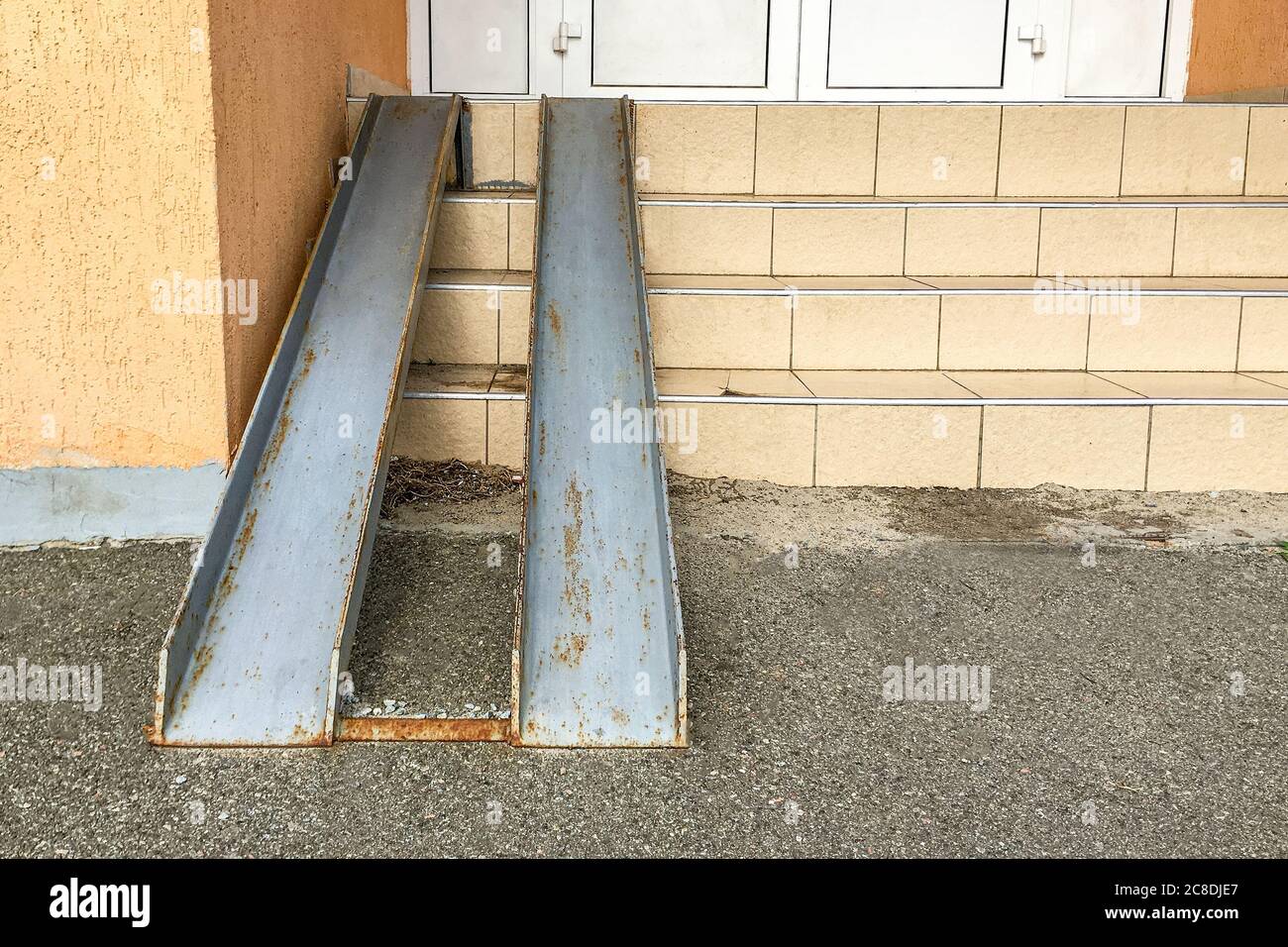 Old rusty metal ramp for entry of wheelchairs and baby carriage, over steps in residential building. People protection. Close-up. Outdoors. Stock Photo