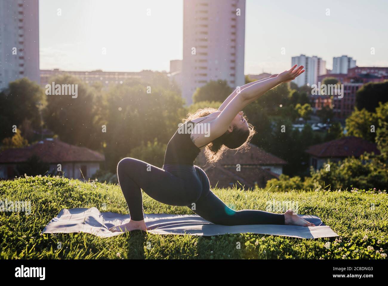 Young woman practicing yoga in warrior position at city park during sunny day Stock Photo