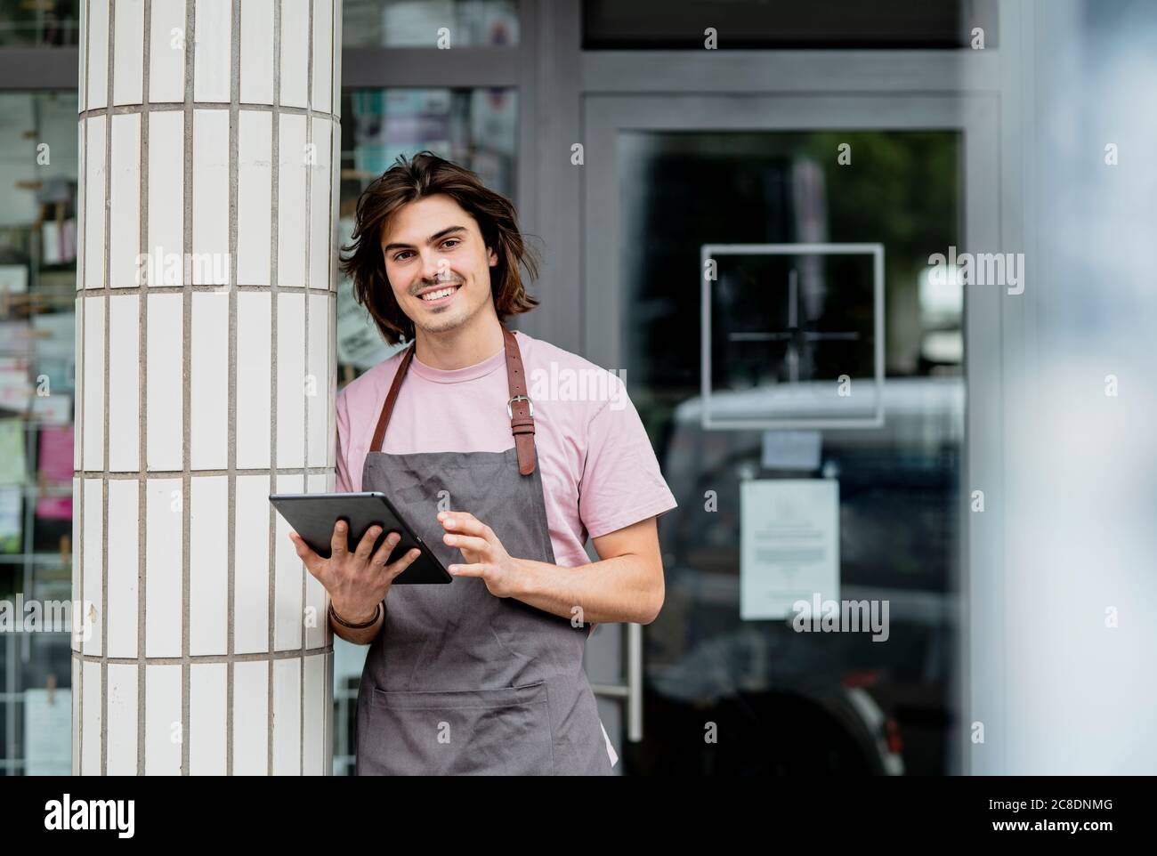 Smiling owner using digital tablet while standing by column against cafe Stock Photo