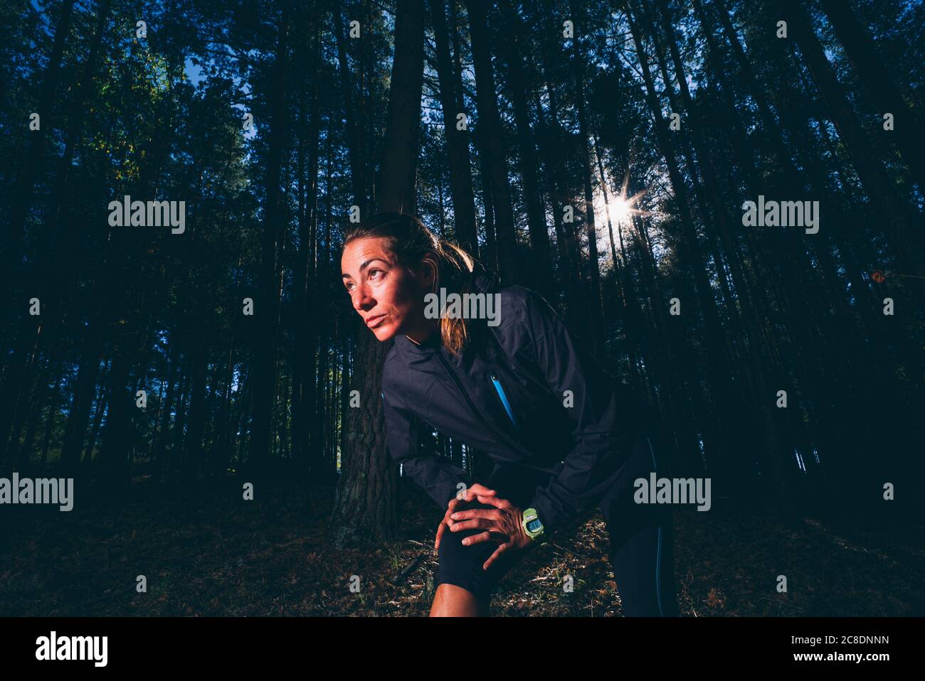 Woman looking away while exercising against trees in forest Stock Photo ...