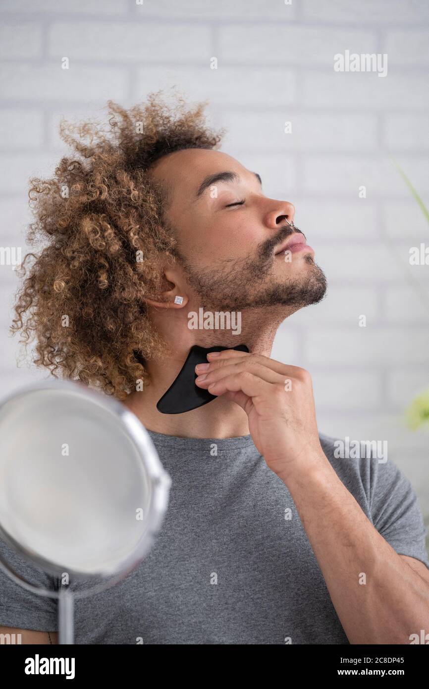 Close-up of young man massaging neck with gua sha stone at home Stock Photo