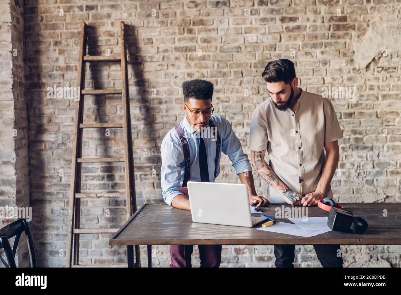 Two creative businessmen using laptop in loft office Stock Photo