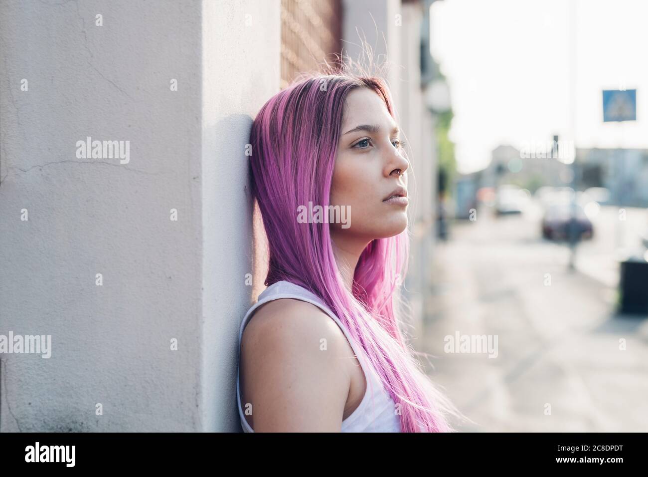 Portrait of a stylish young woman with pink hair leaning against a wall ...