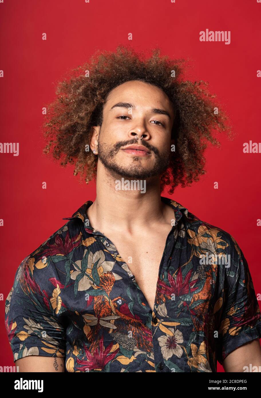 Handsome young man with curly hair standing against red background Stock Photo