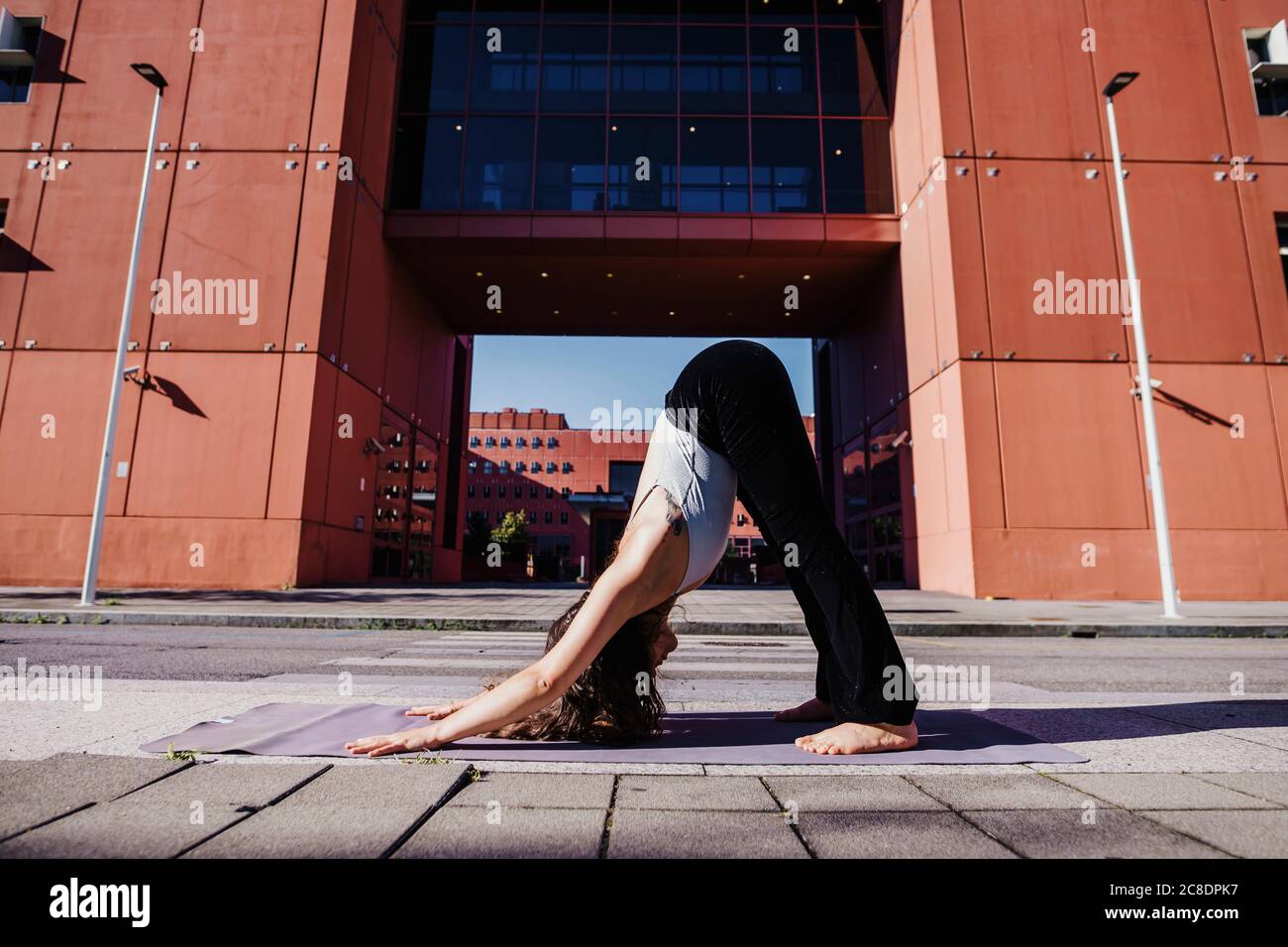 Young woman performing yoga in downward facing dog position on city street Stock Photo