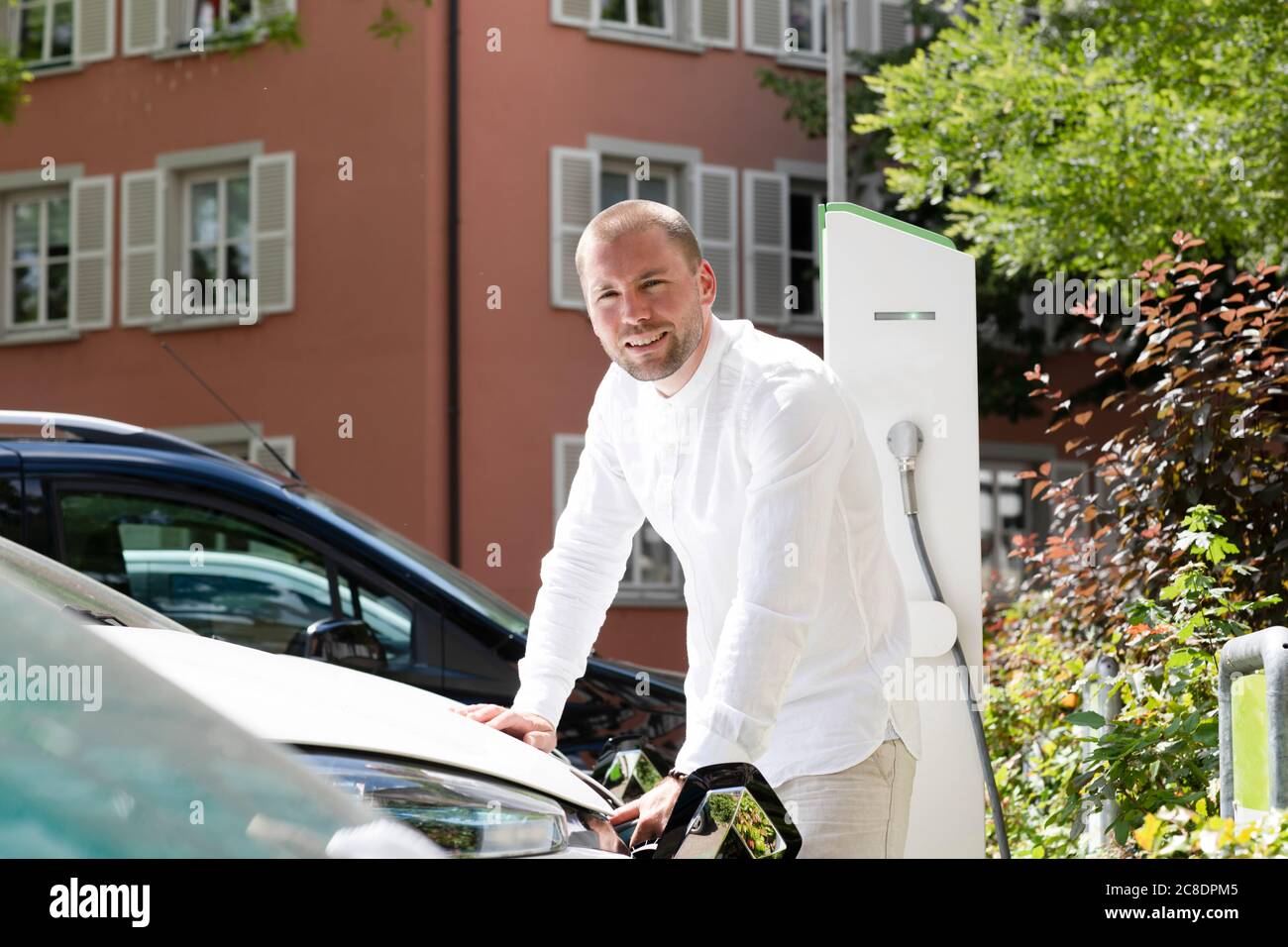 Smiling mid adult man charging electric car at station Stock Photo
