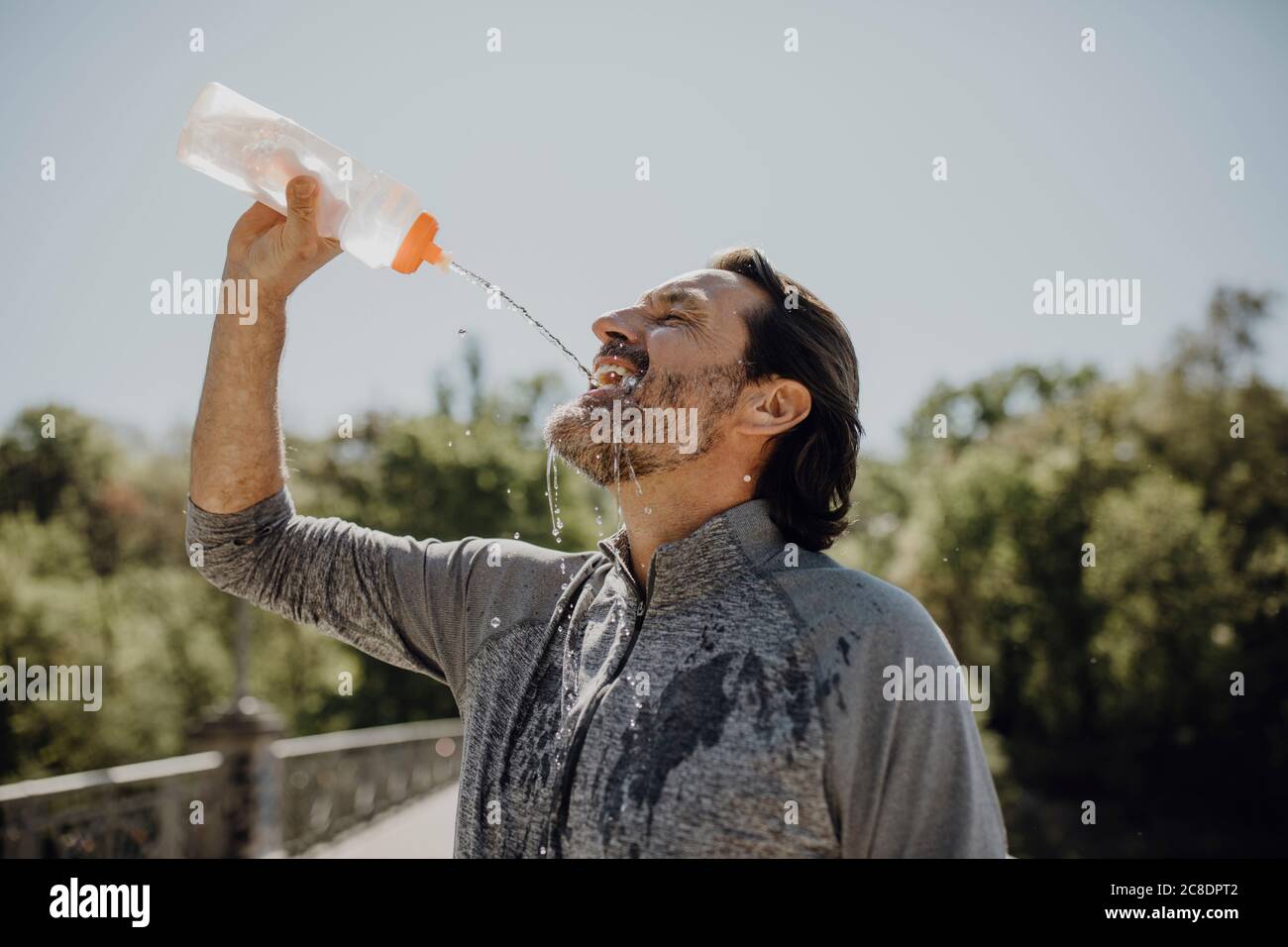 Close-up of mature man drinking water while standing against clear sky in park Stock Photo