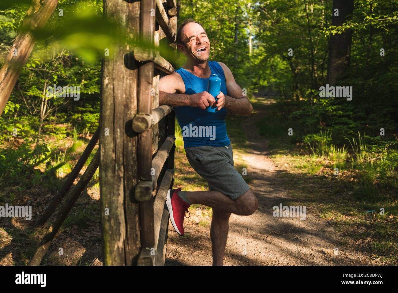 Happy man looking away while standing with water bottle against wood at park Stock Photo