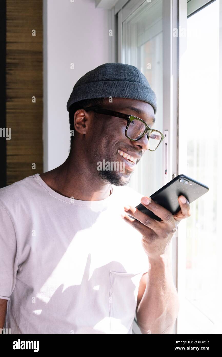 Happy young man using smart phone by window Stock Photo