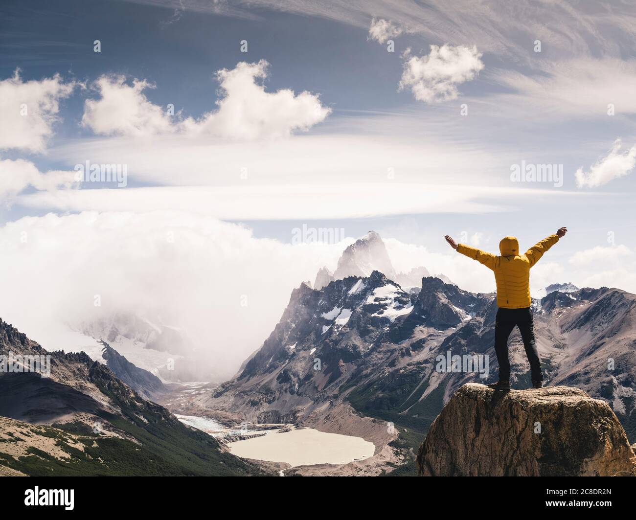 Man with arms outstretched looking at snowcapped mountain against cloudy sky, Patagonia, Argentina Stock Photo