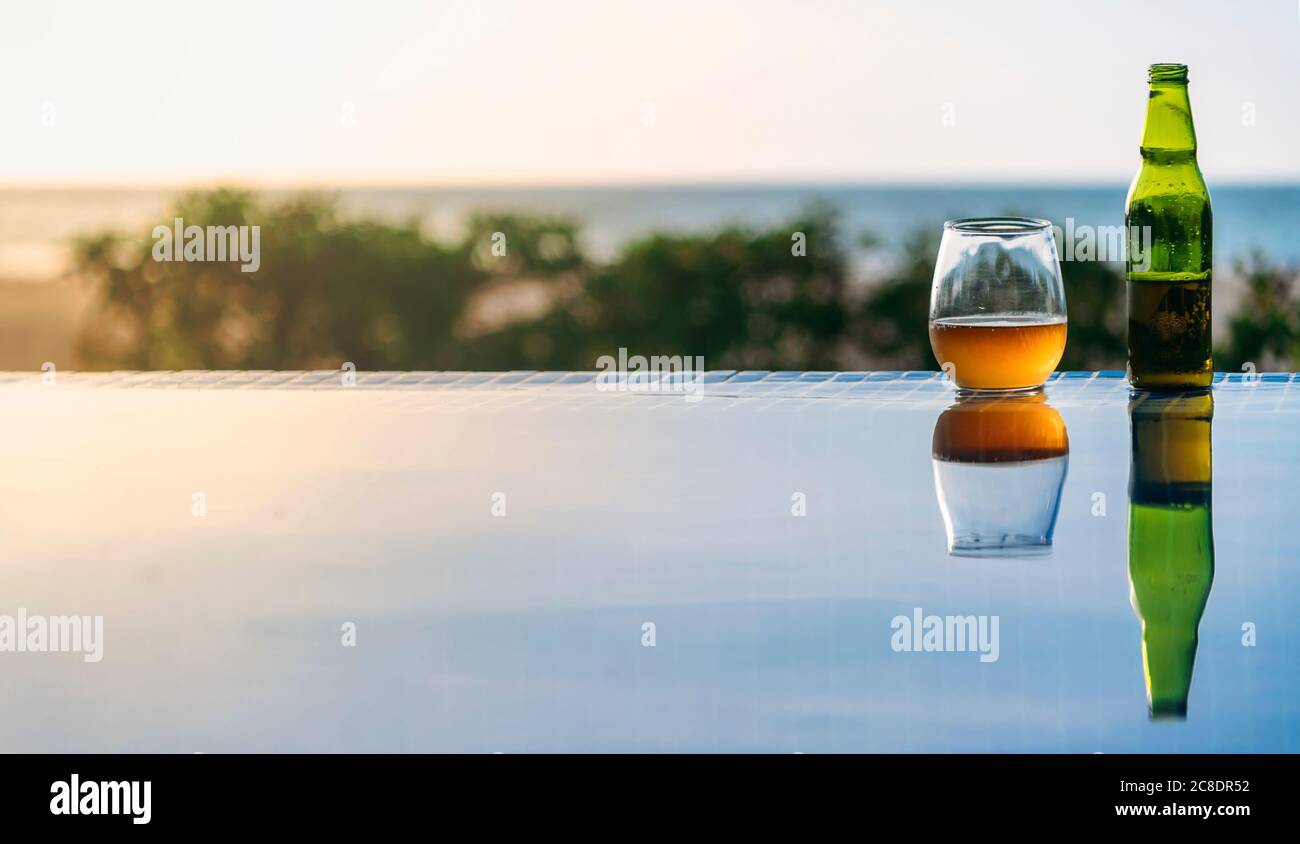 Open beer left at edge of outdoor swimming pool in summer Stock Photo