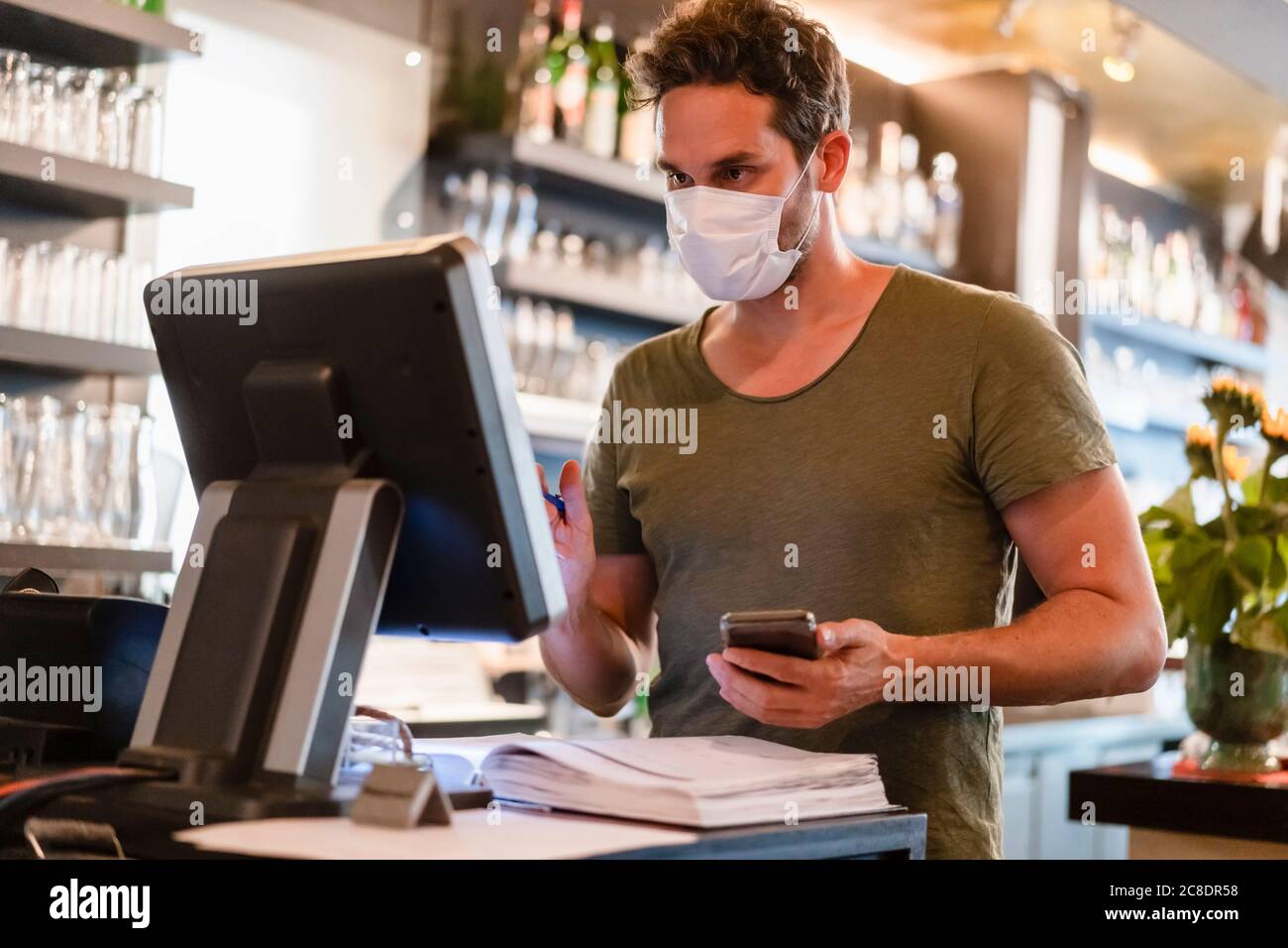 Restaurant manager with protective mask using computer and smartphone Stock Photo