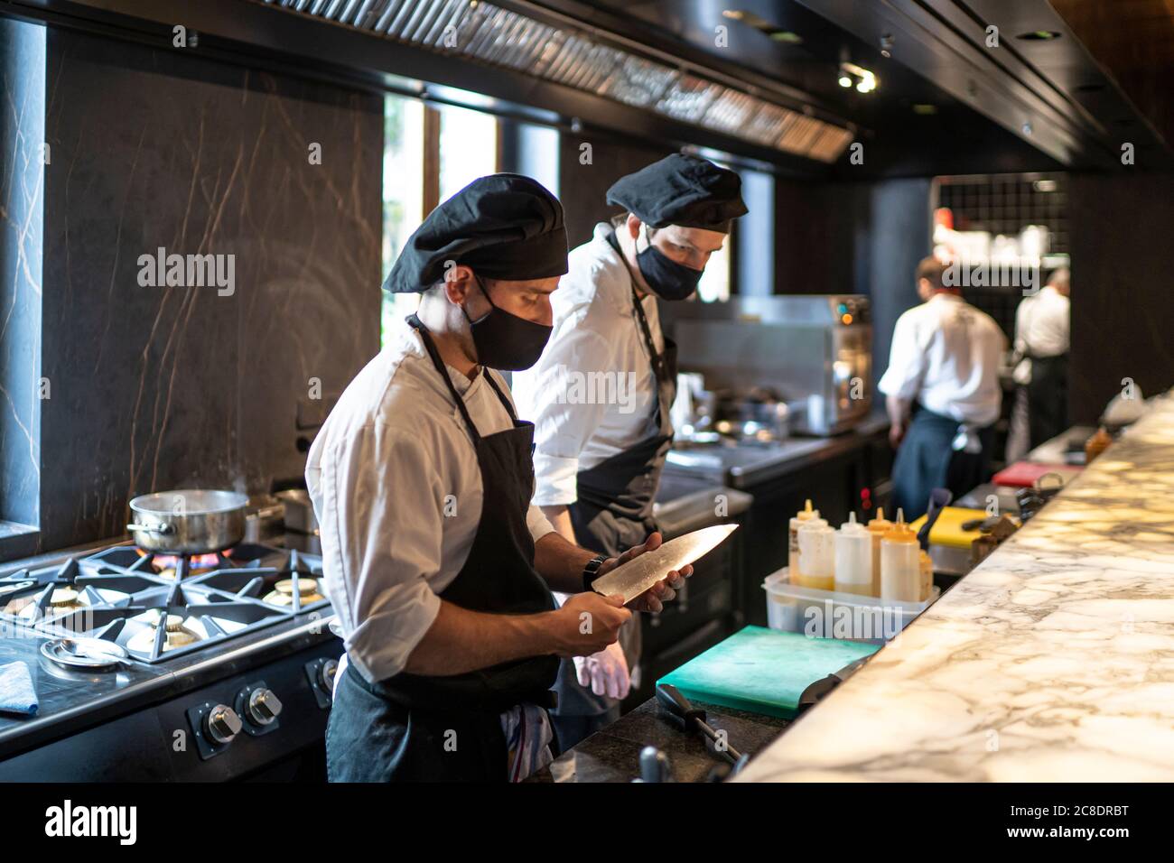 Chefs wearing protective face masks working together in restaurant kitchen Stock Photo