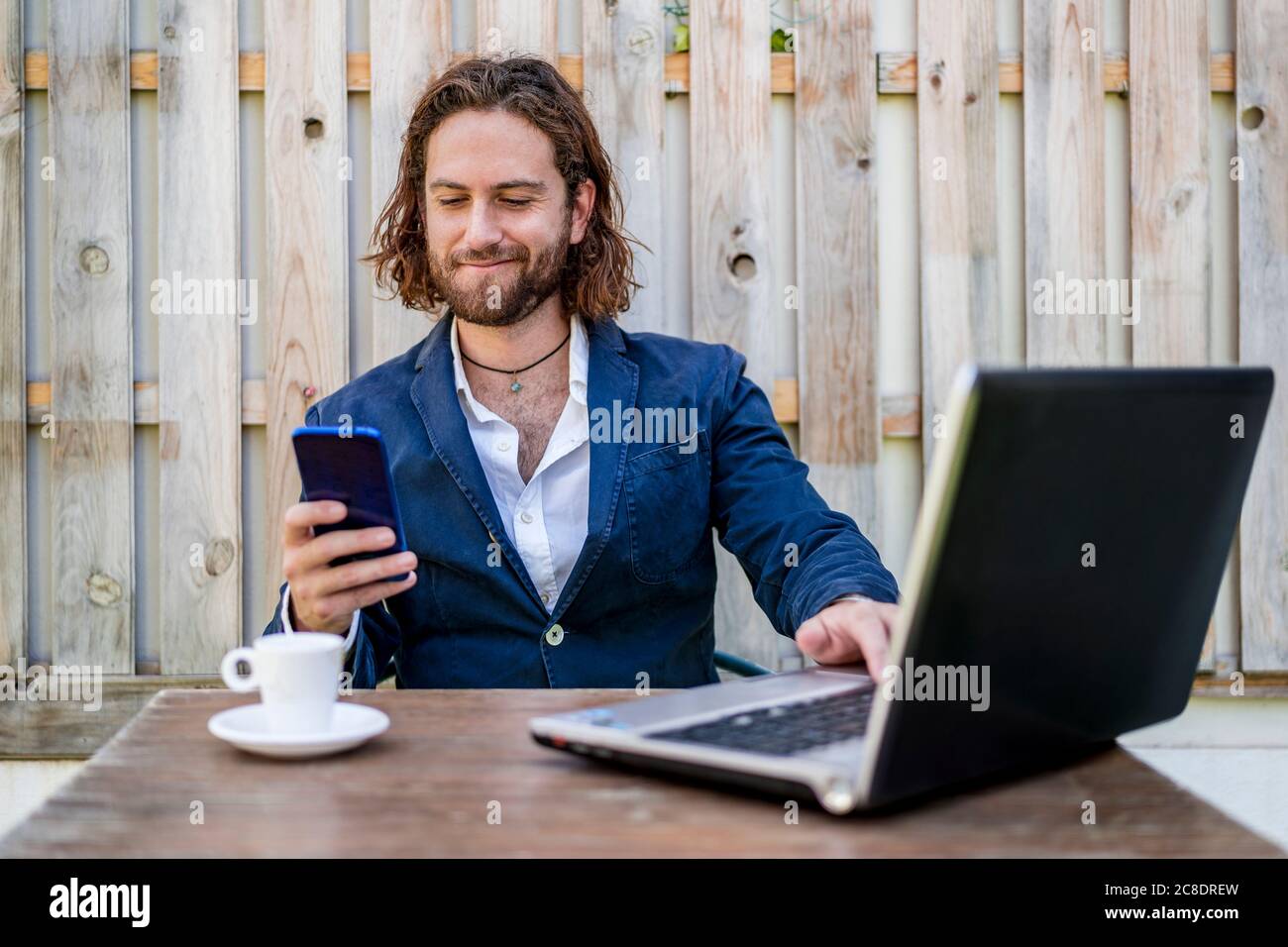 Businessman smirking while using mobile phone sitting at cafe Stock Photo