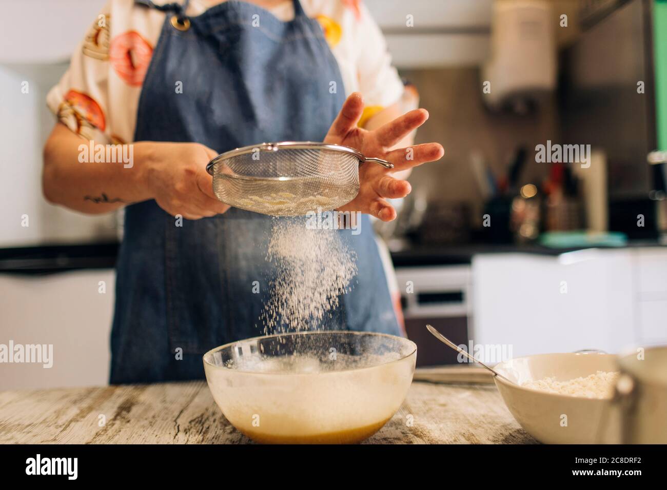 Close-up of female baker sifting flour in batter on table at workshop Stock Photo