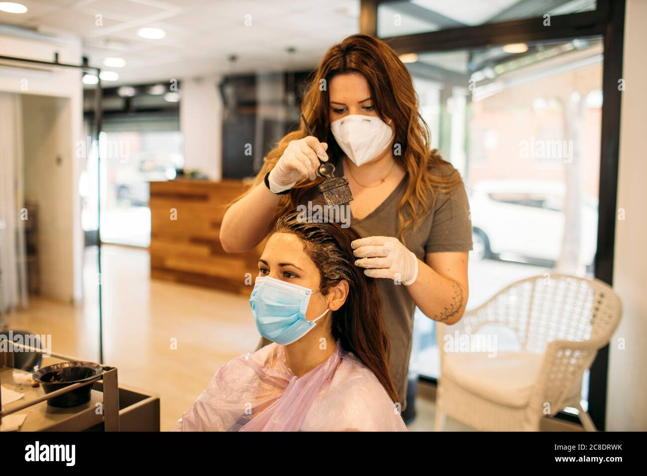 Female hairdresser with mask staining hair of female customer with mask