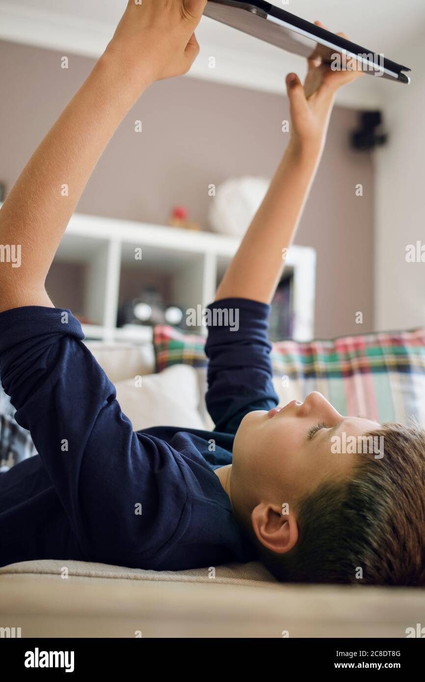Boy playing games on digital tablet while lying on sofa at home Stock ...