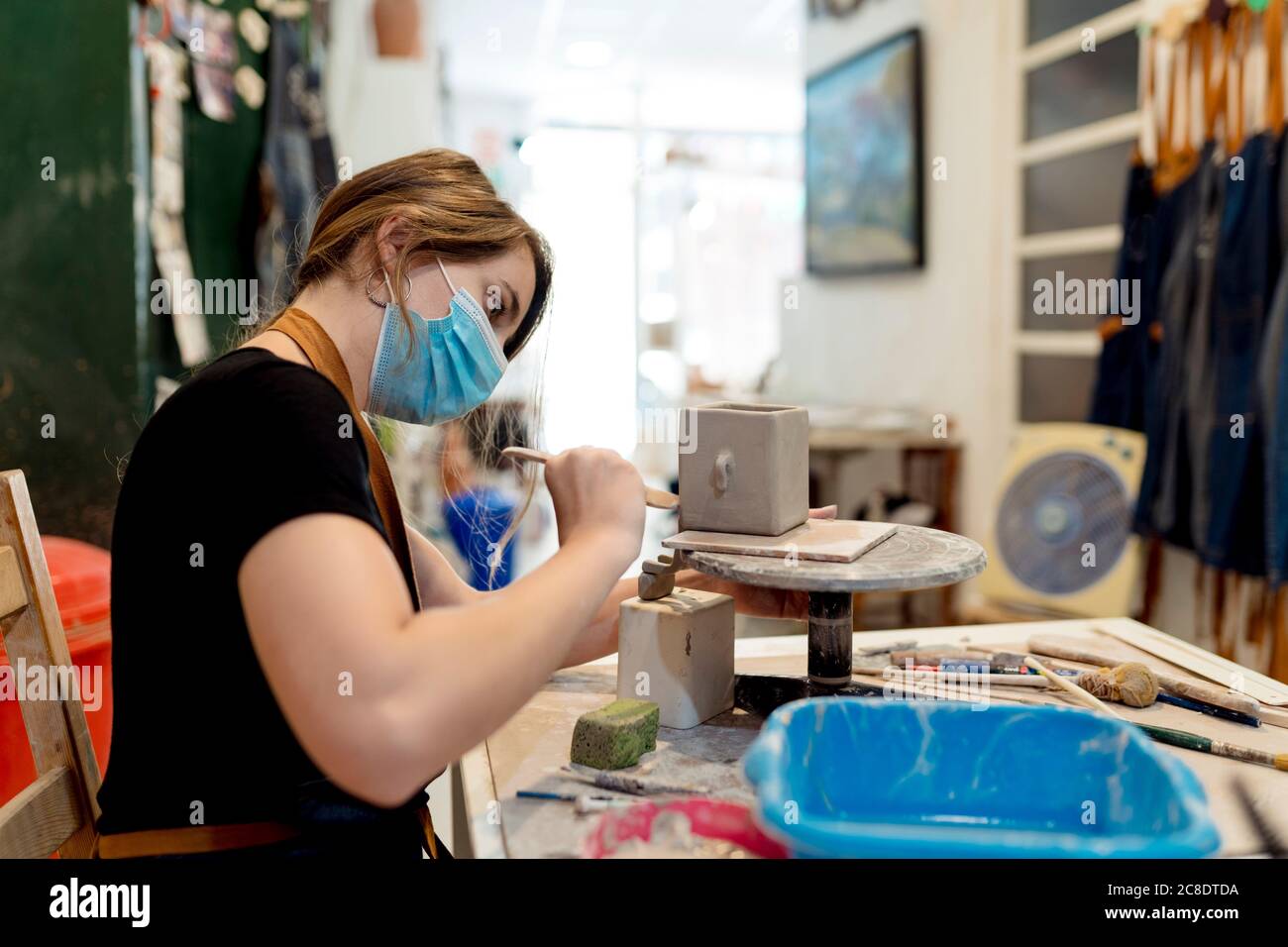 Young woman wearing mask making ceramic on workbench in workshop Stock Photo