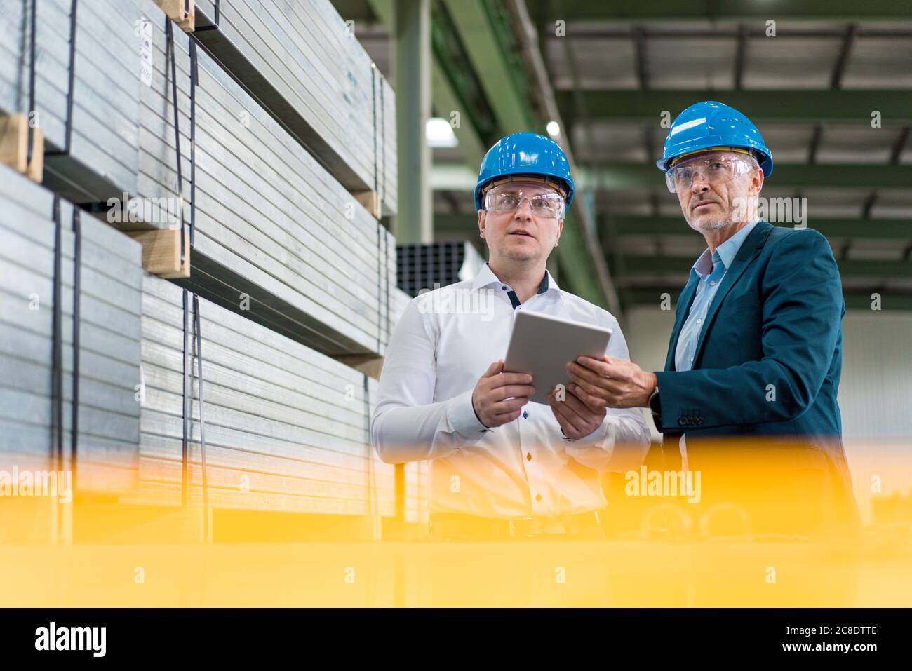 Two businessmen wearing hard hats and safety goggles in a factory using tablet Stock Photo