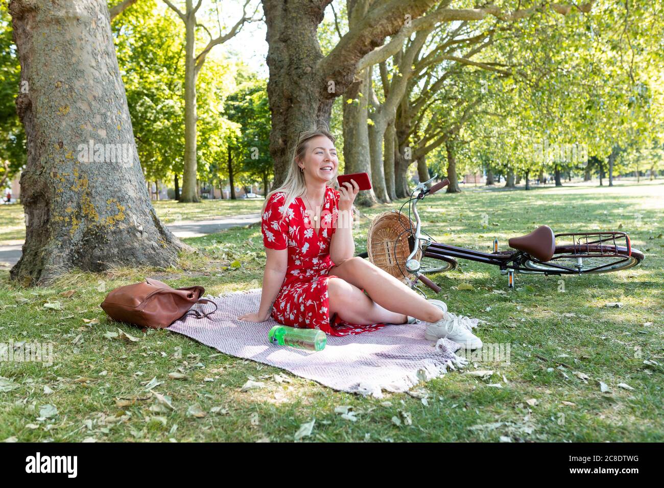 Happy woman holding smart phone while sitting on blanket at public park Stock Photo