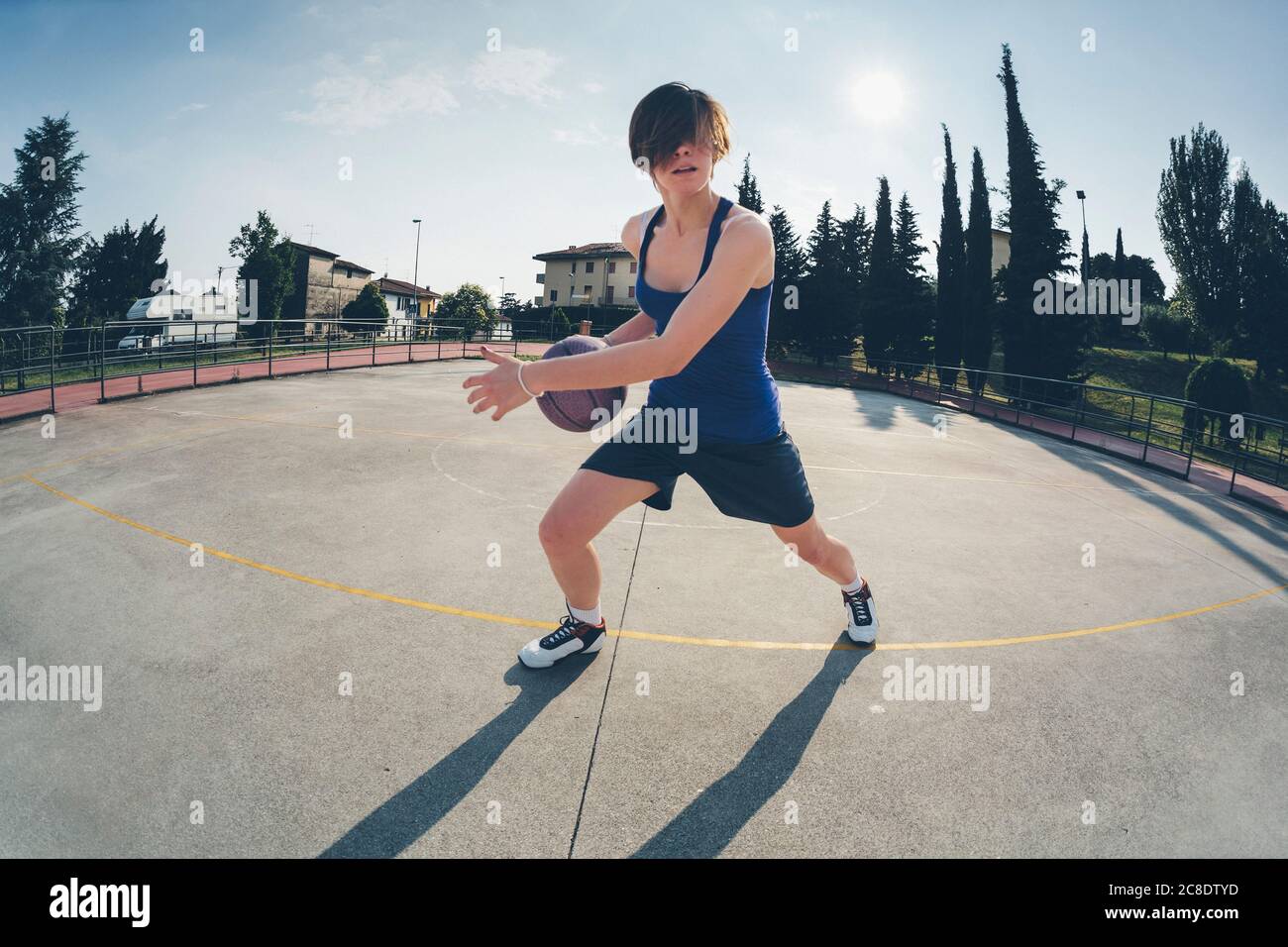 Teenage girl practicing basketball on court against sky Stock Photo