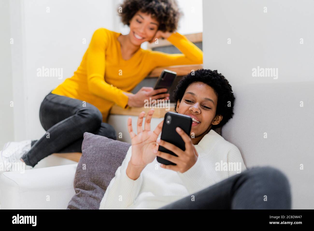 Two young women relaxing at home using their smartphones Stock Photo