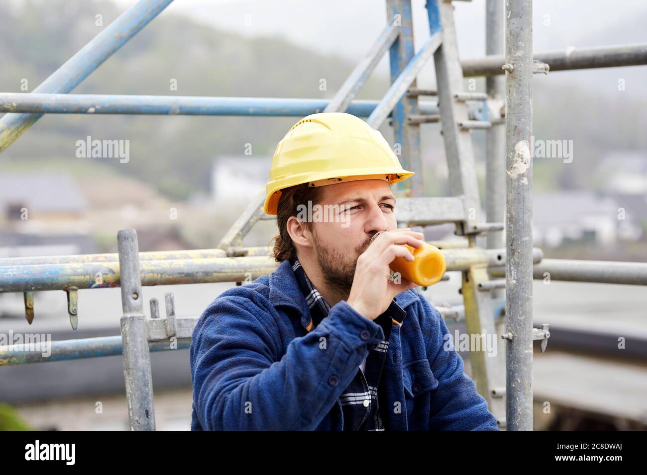 Worker drinking juice on scaffolding on a construction site Stock Photo