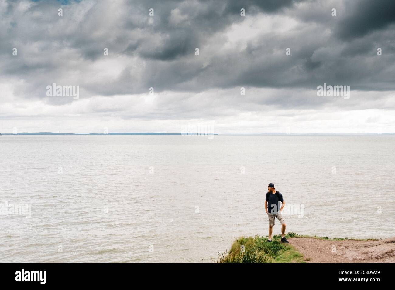 Man standing on cliff while looking at sea against storm clouds Stock Photo