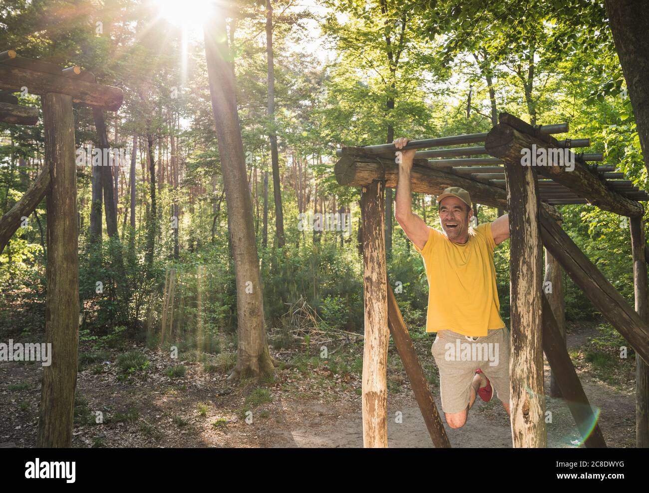 Cheerful mature man exercising while hanging from monkey bars against trees at park Stock Photo