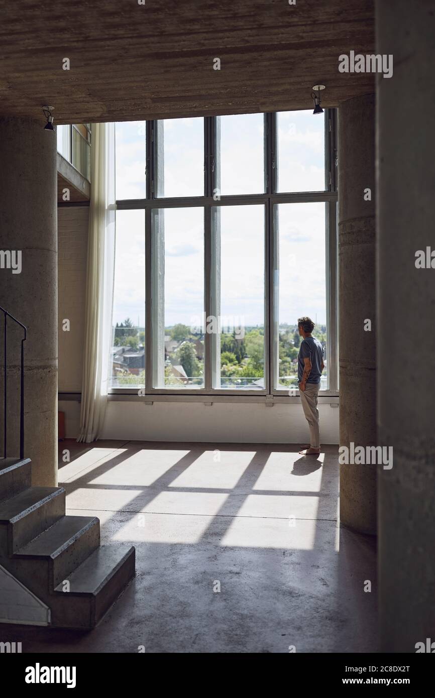 Senior man looking out of window in a loft flat stock photo