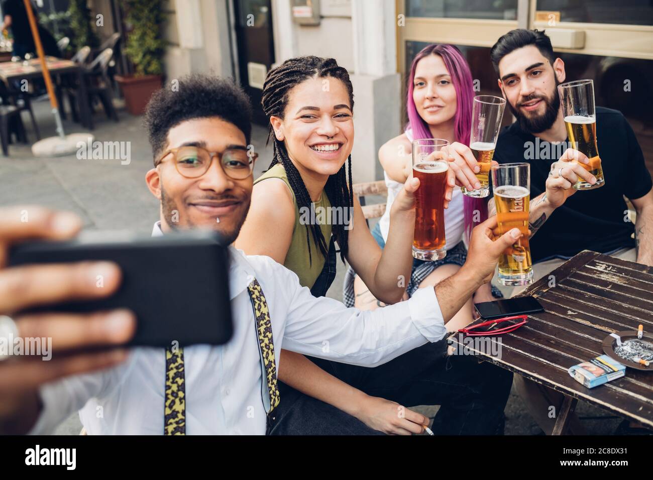 Happy friends holsing beer glasses and taking a selfie outdoors at a bar Stock Photo