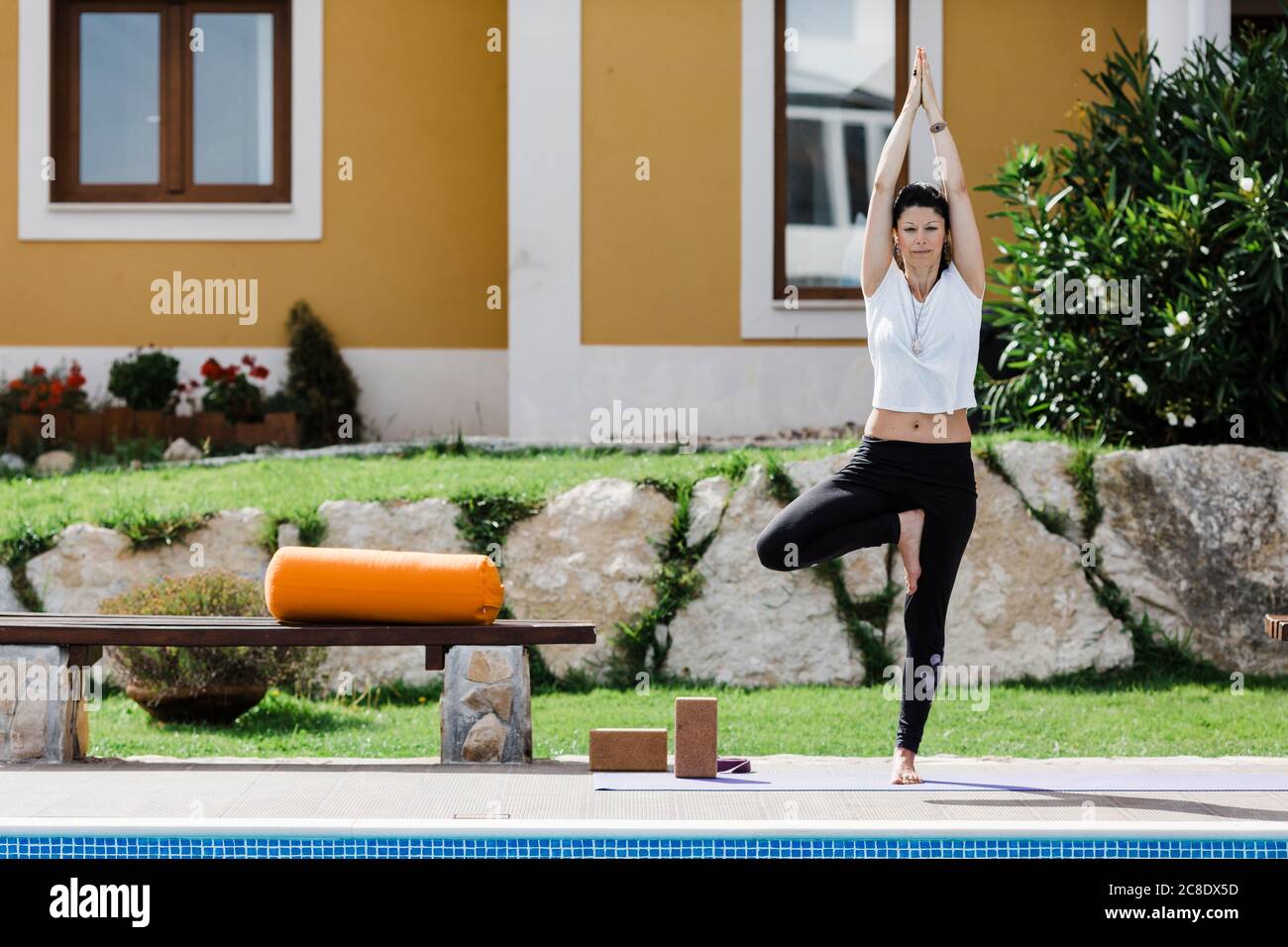 Woman practicing tree position at poolside against house in garden Stock Photo