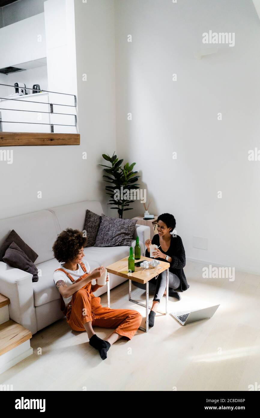 Friends sitting on the floor at home eating Asian food and drinking beer Stock Photo