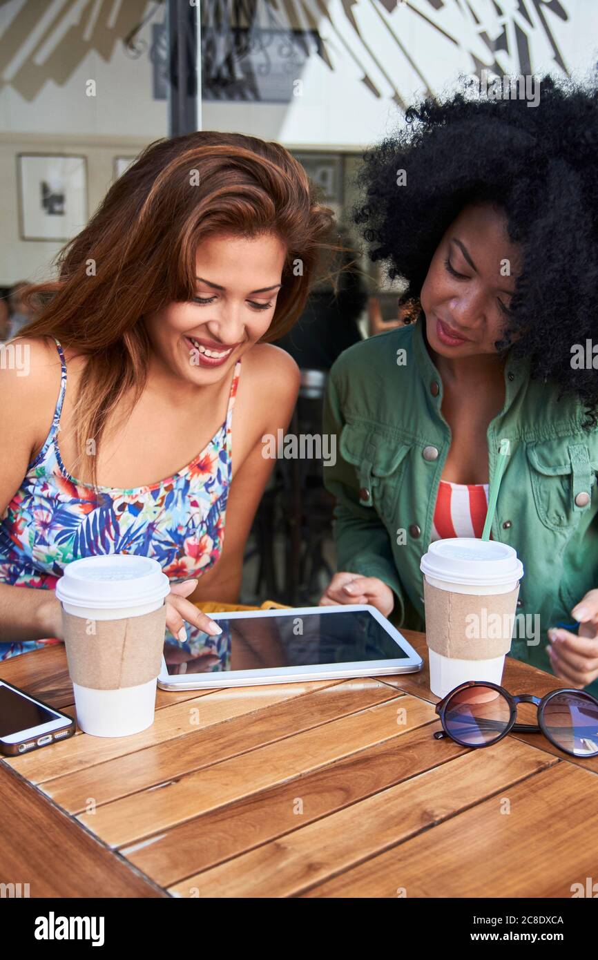 Girlfriends with coffee to go using tablet in cafe Stock Photo