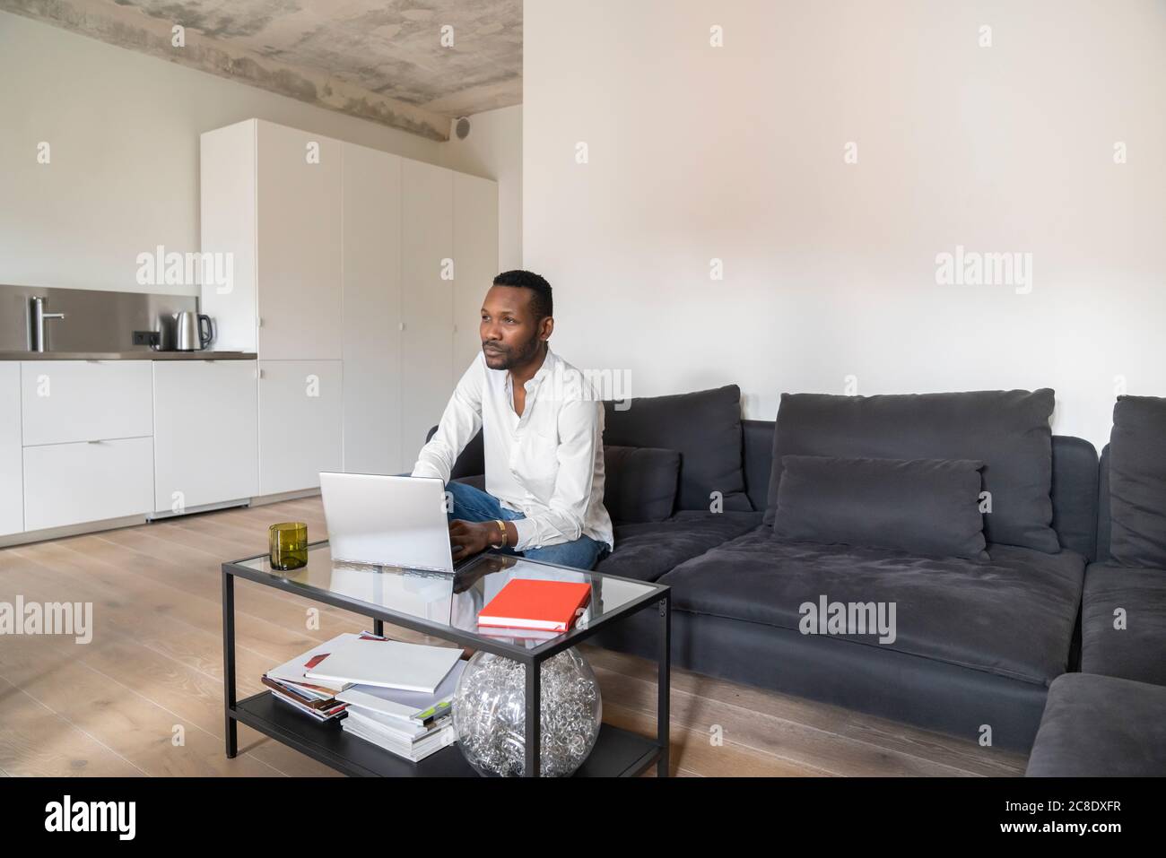 Pensive man sitting on couch in modern apartment using laptop Stock Photo