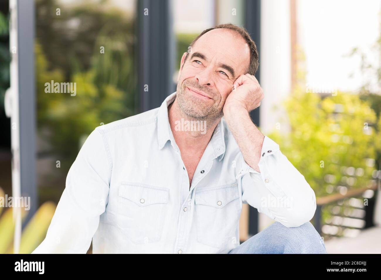 Thoughtful mature man looking away while sitting at back yard Stock Photo