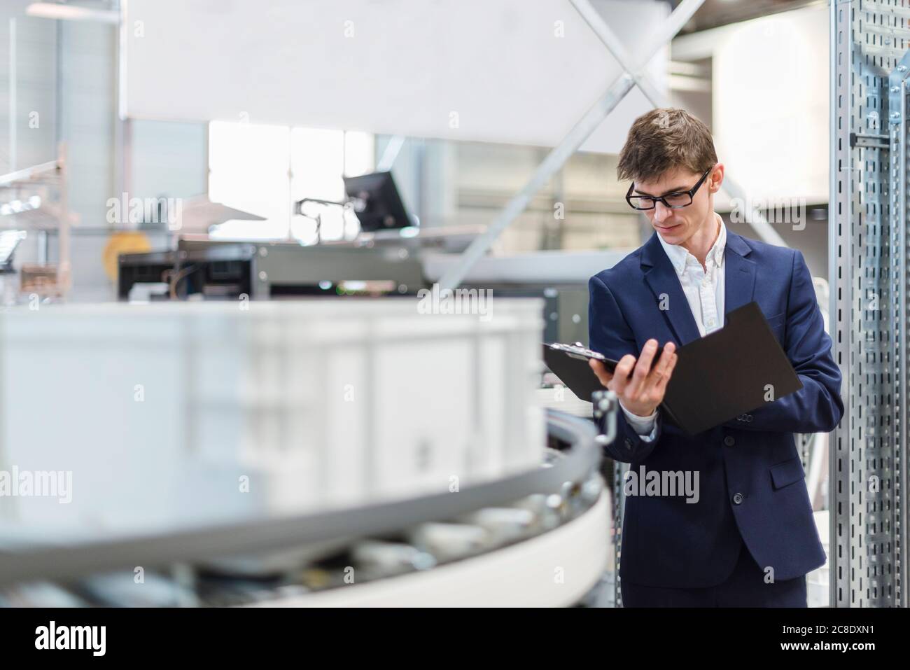 Male manager holding file while standing by production line in factory Stock Photo