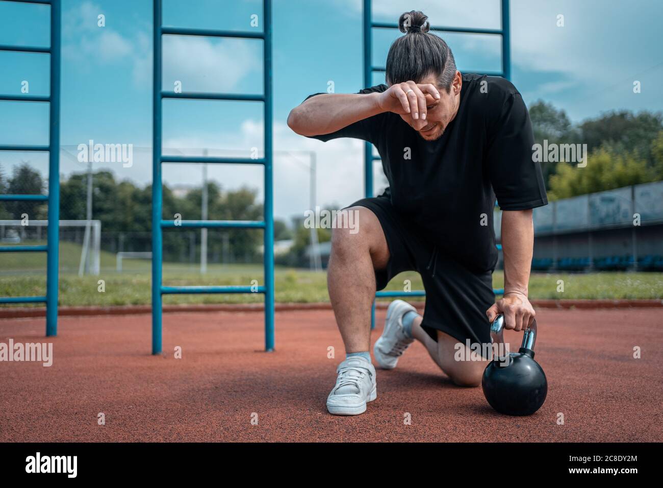 exhausted man athlete taking break between exercising with kettlebell outdoor Stock Photo