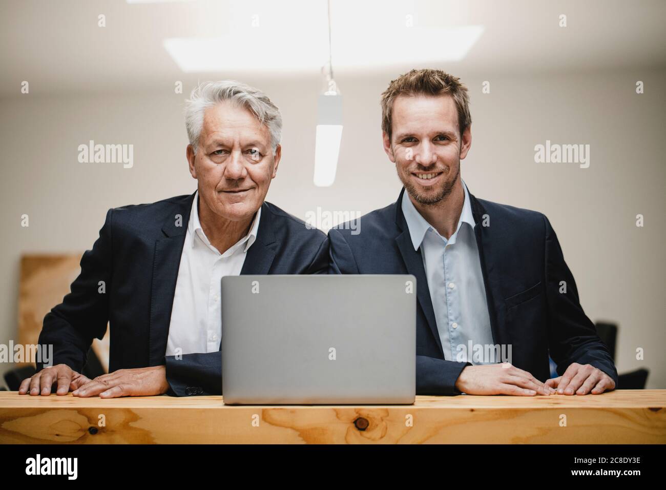 Two confident businessmen sitting in office, using laptop, smiling Stock Photo