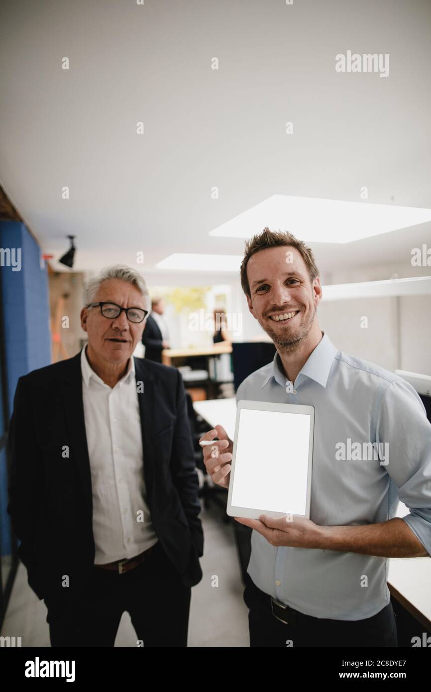 Two successful businessmen standing in office, using digital tablet Stock Photo