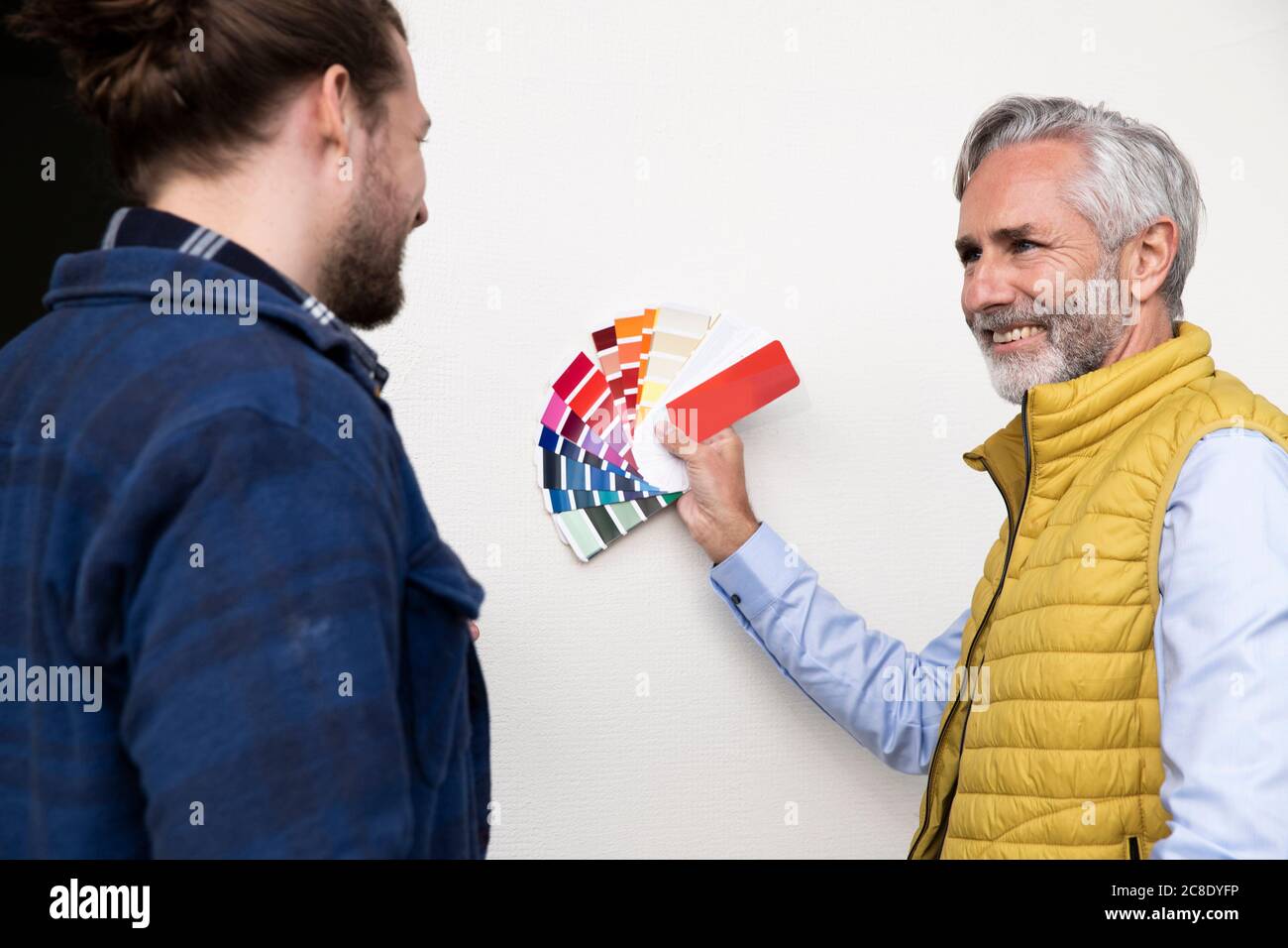 Male architect showing color swatches to construction worker while standing by wall in house Stock Photo