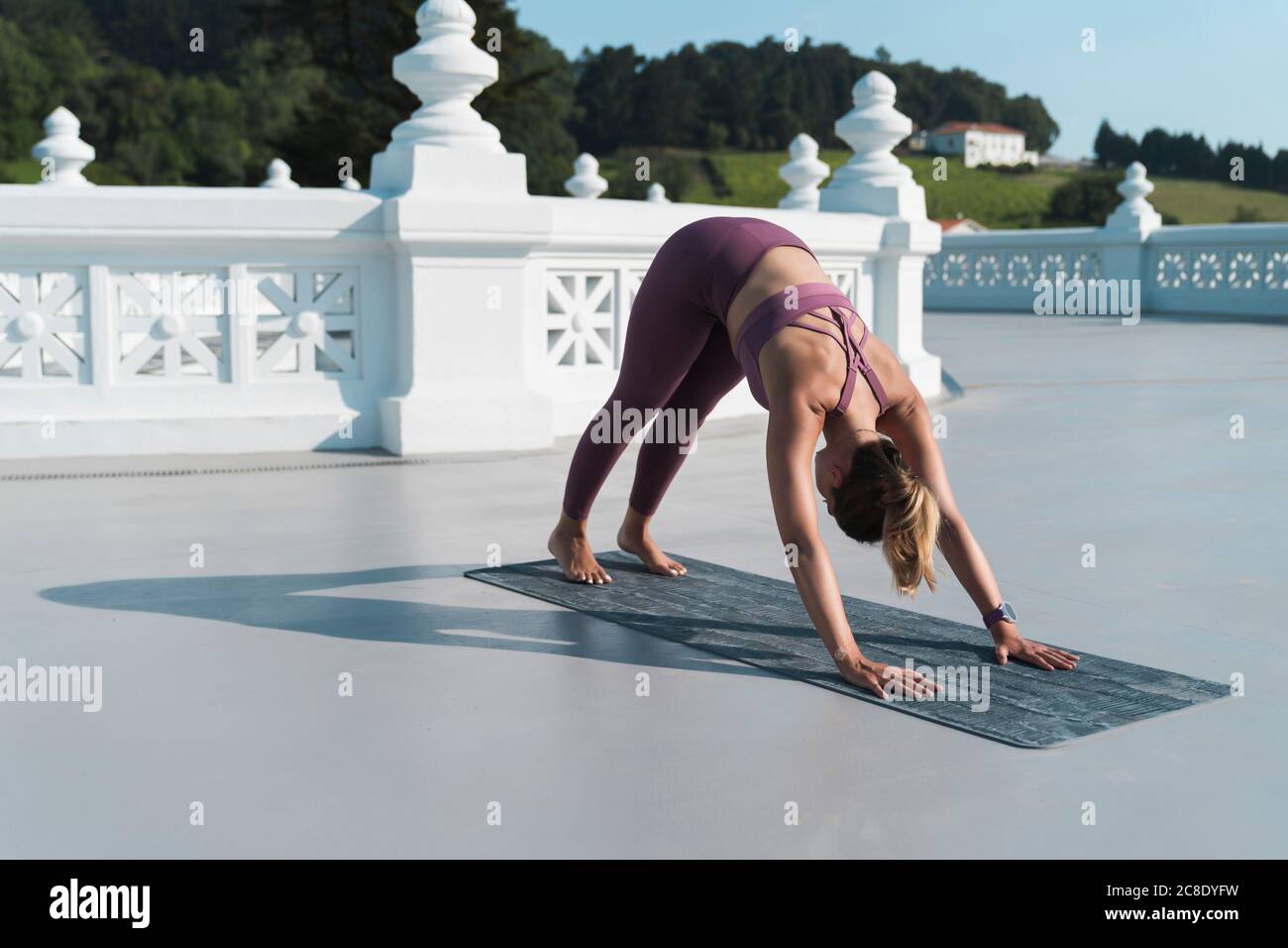 Young woman practicing downward facing dog position on mat over building terrace Stock Photo